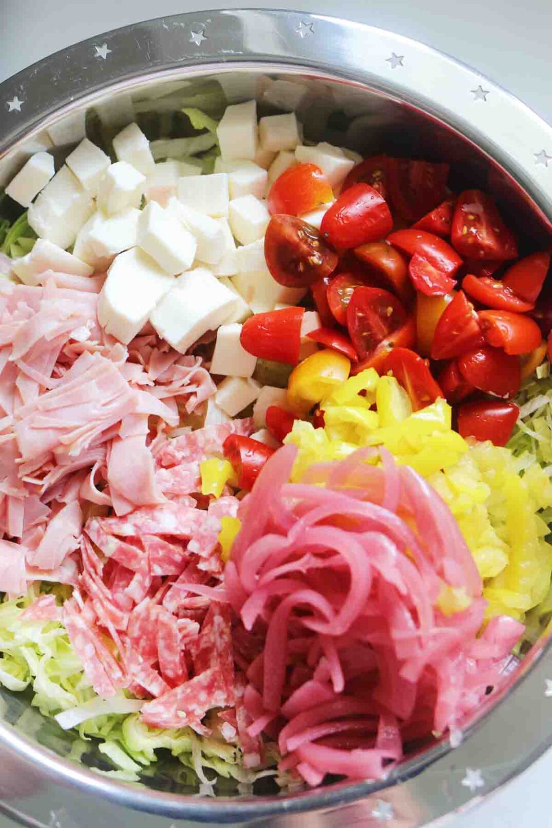 chopped up italian cold cuts and colorful veggies in a silver bowl with shredded lettuce.