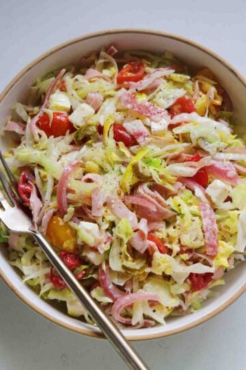 an overhead view of a chopped grinder salad in a white bowl and a white countertop.