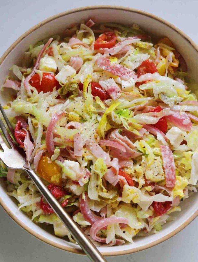 an overhead view of a chopped grinder salad in a white bowl and a white countertop.