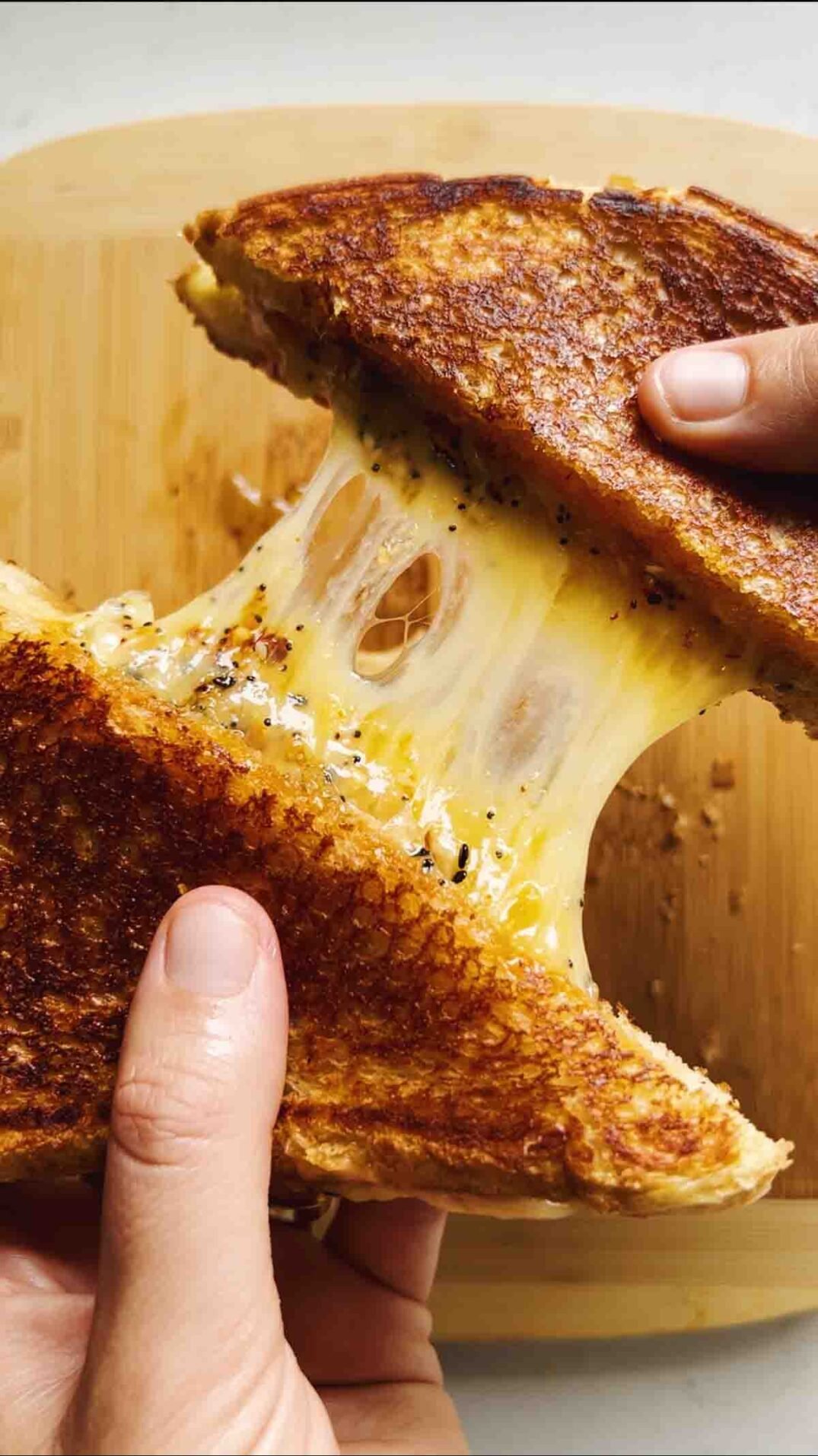 a grilled cheese pull over a wooden cutting board on a white countertop.