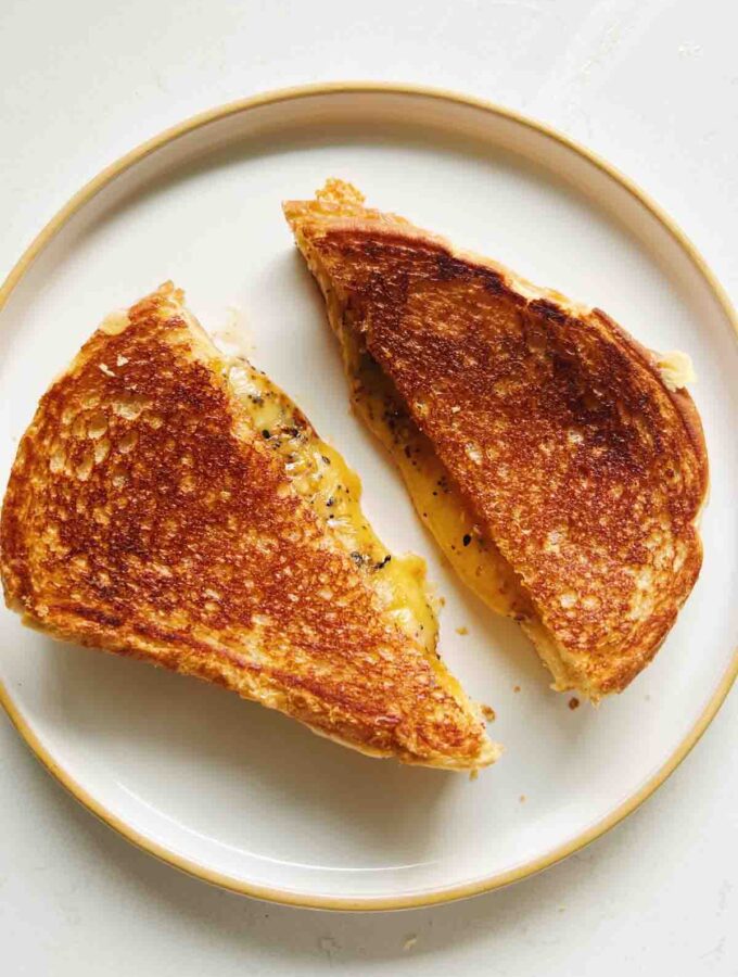 a diagonally cut grilled cheese on a white plate with cheese oozing out.