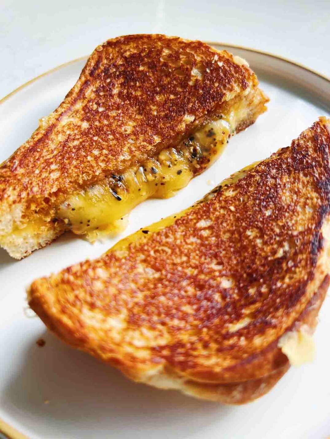 a side angle of a golden grilled cheese cut in half on a white plate.