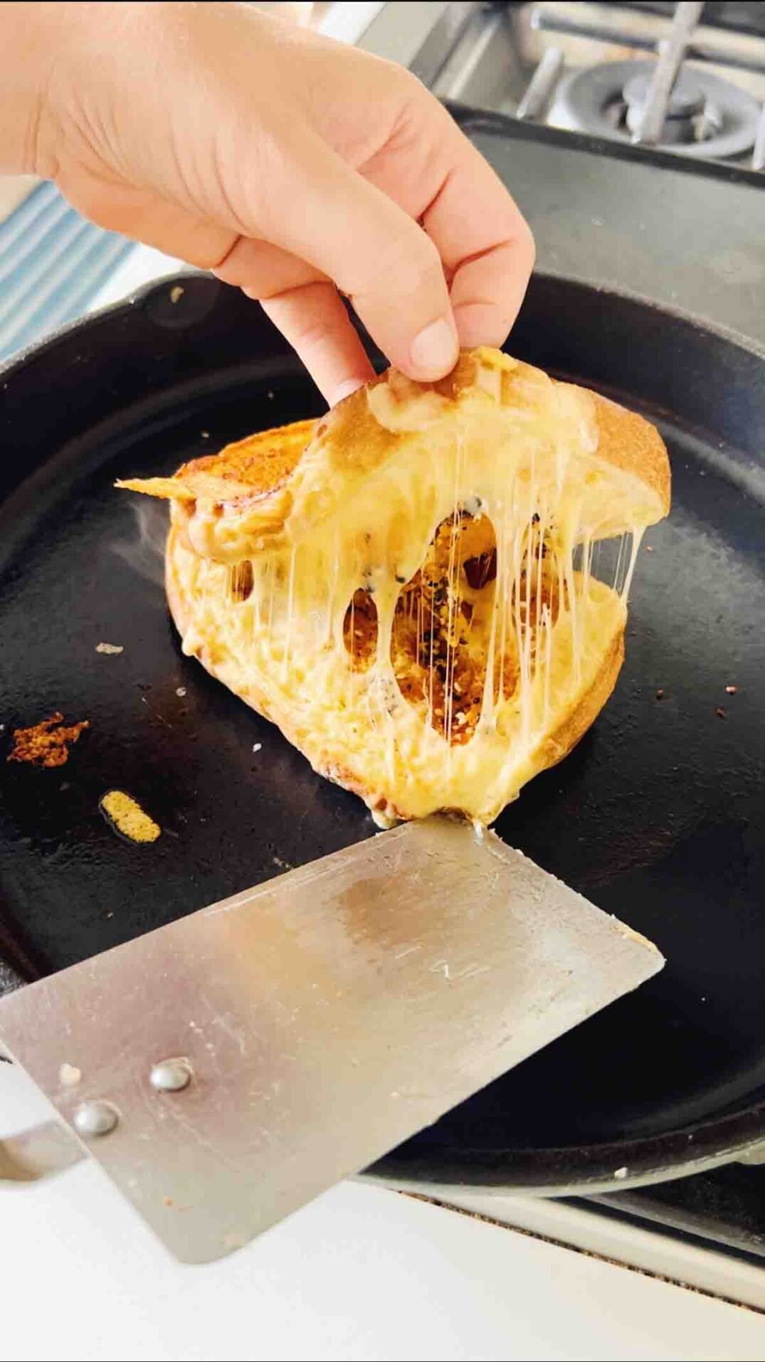 a hand opening up a grilled cheese with the cheese stretching.