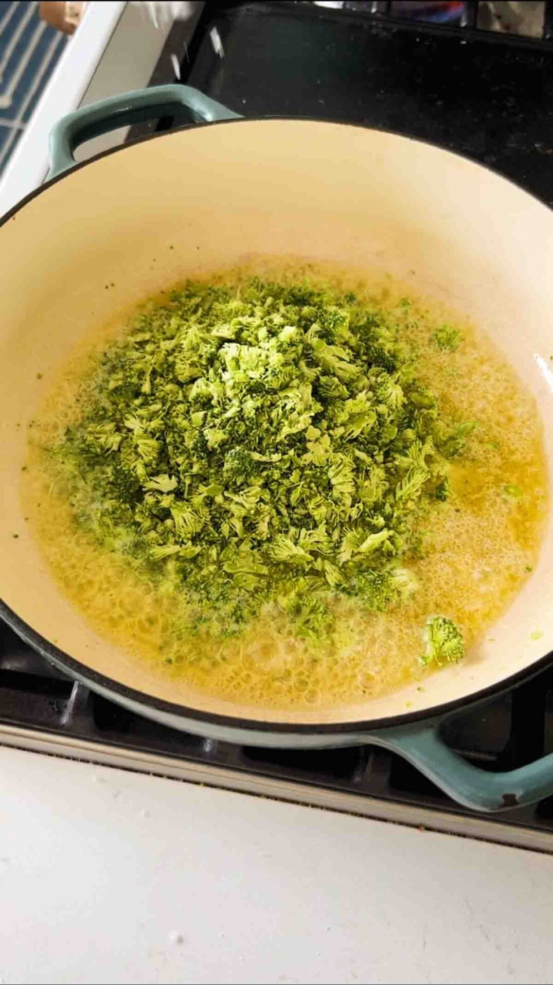 chopped broccoli in butter in a blue braising pan.