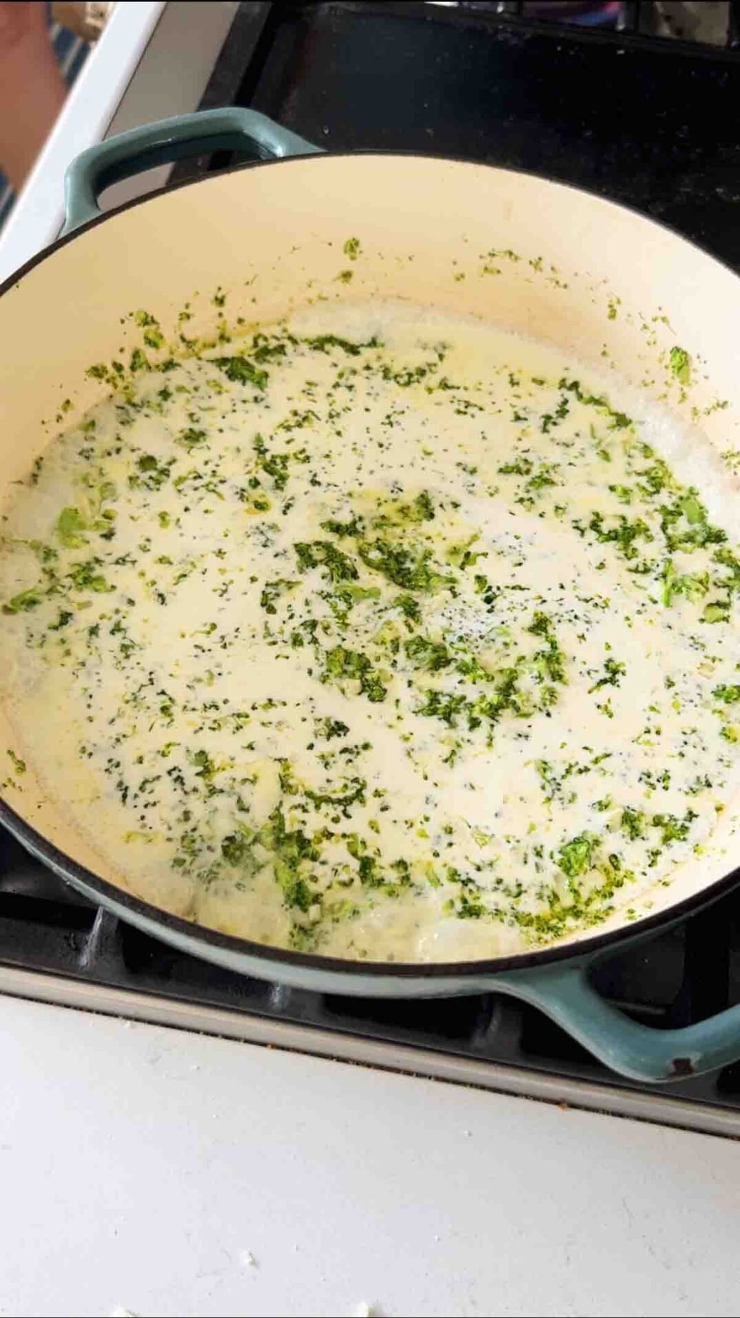 lemon cream sauce with broccoli in a blue braising dish on a stovetop.