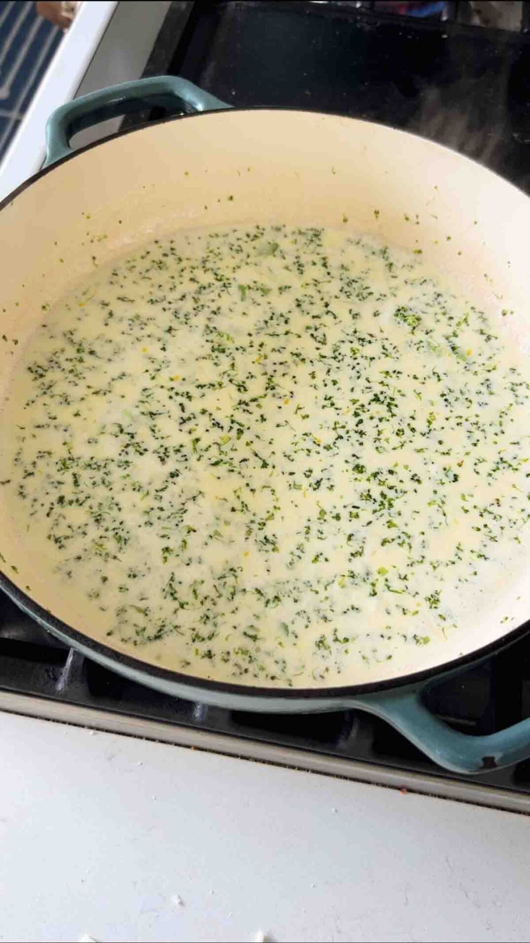 lemon cream sauce with broccoli in a blue braising dish on a stovetop.