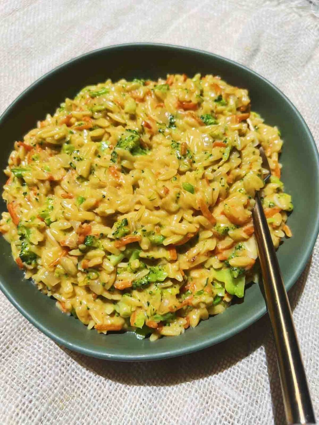 cheesy orzo with broccoli, a for, and a green bowl on a white tablecloth.