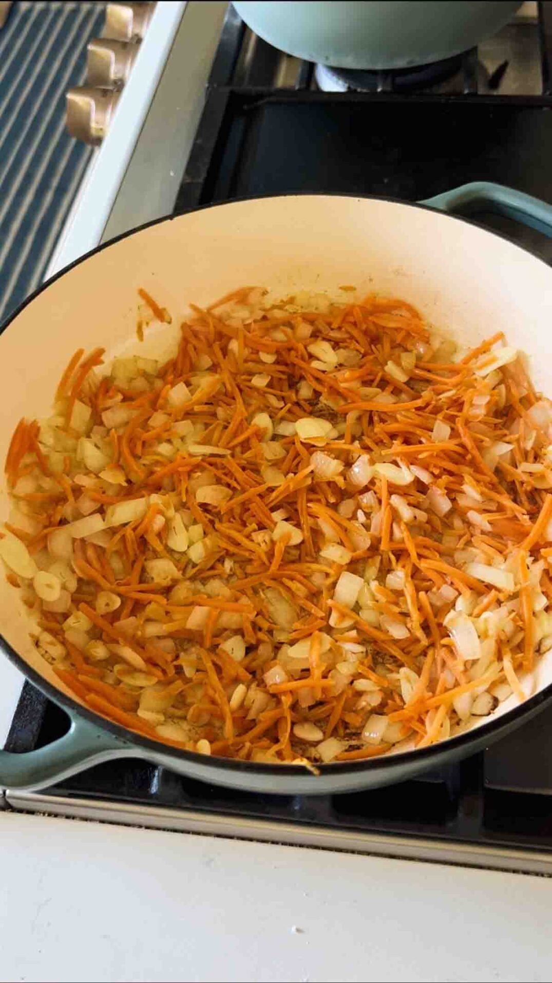 cooked shredded carrots in a blue braising dish on the stovetop.