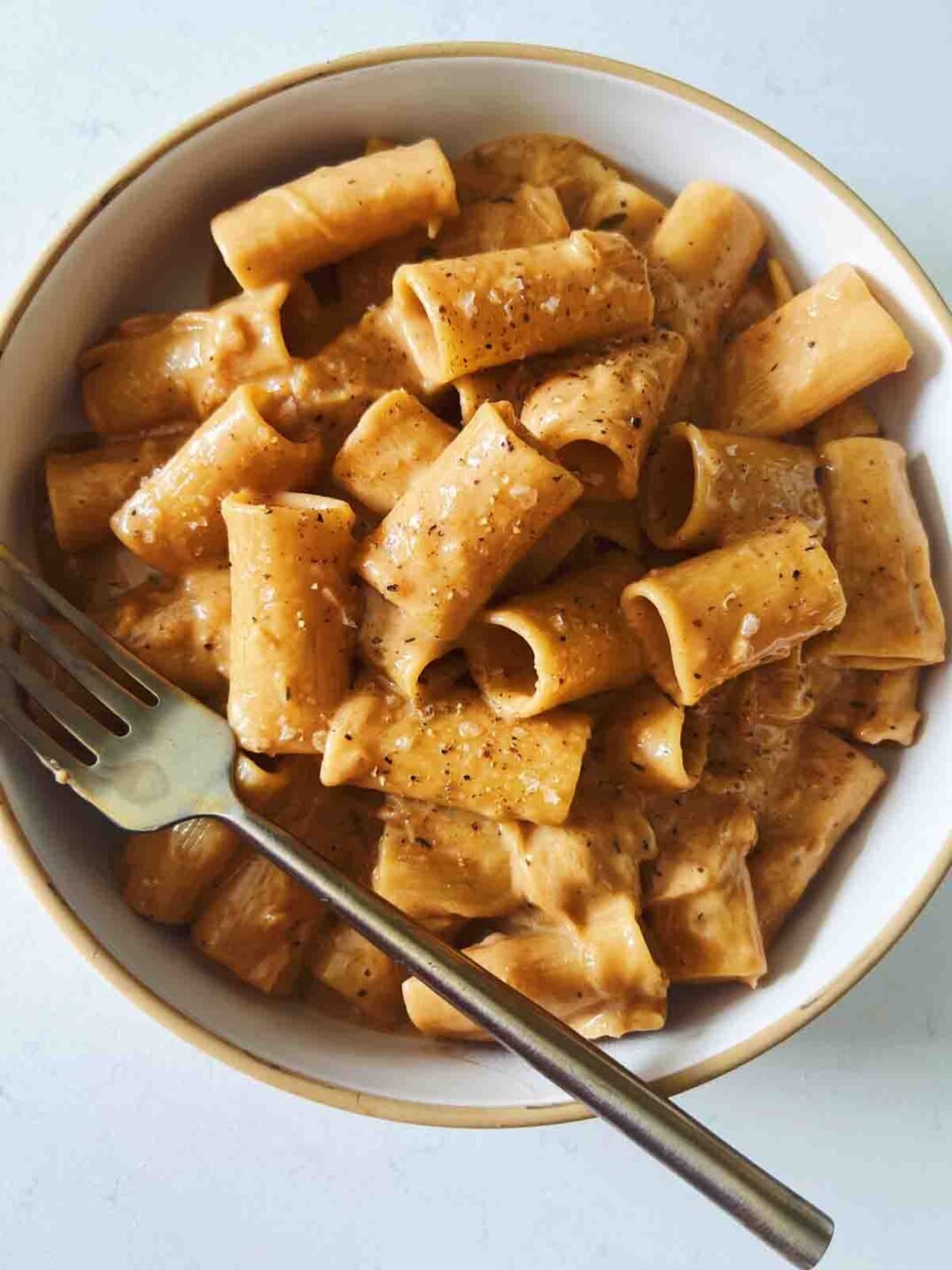viral french onion rigatoni in a white bowl with a golden fork.