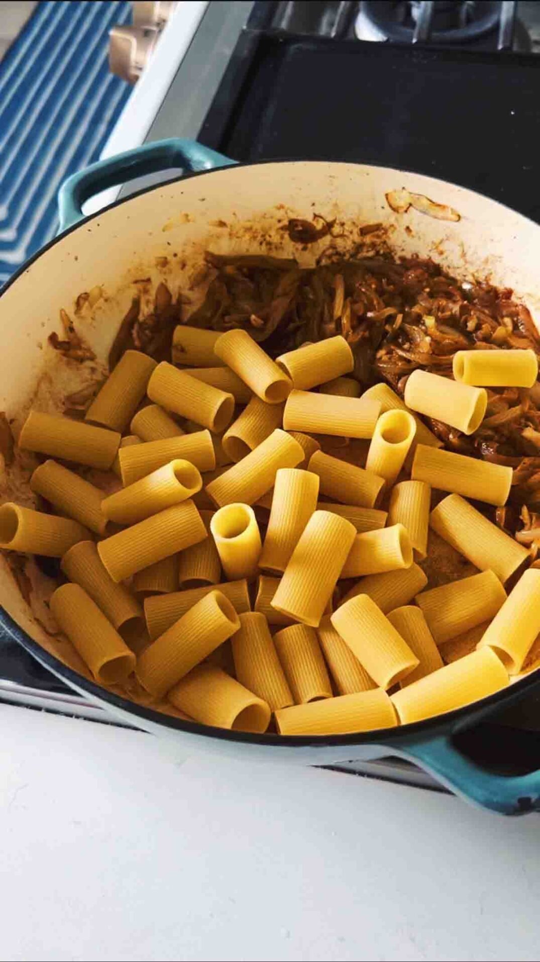 dry rigatoni and caramelized onions in a blue braising dish.