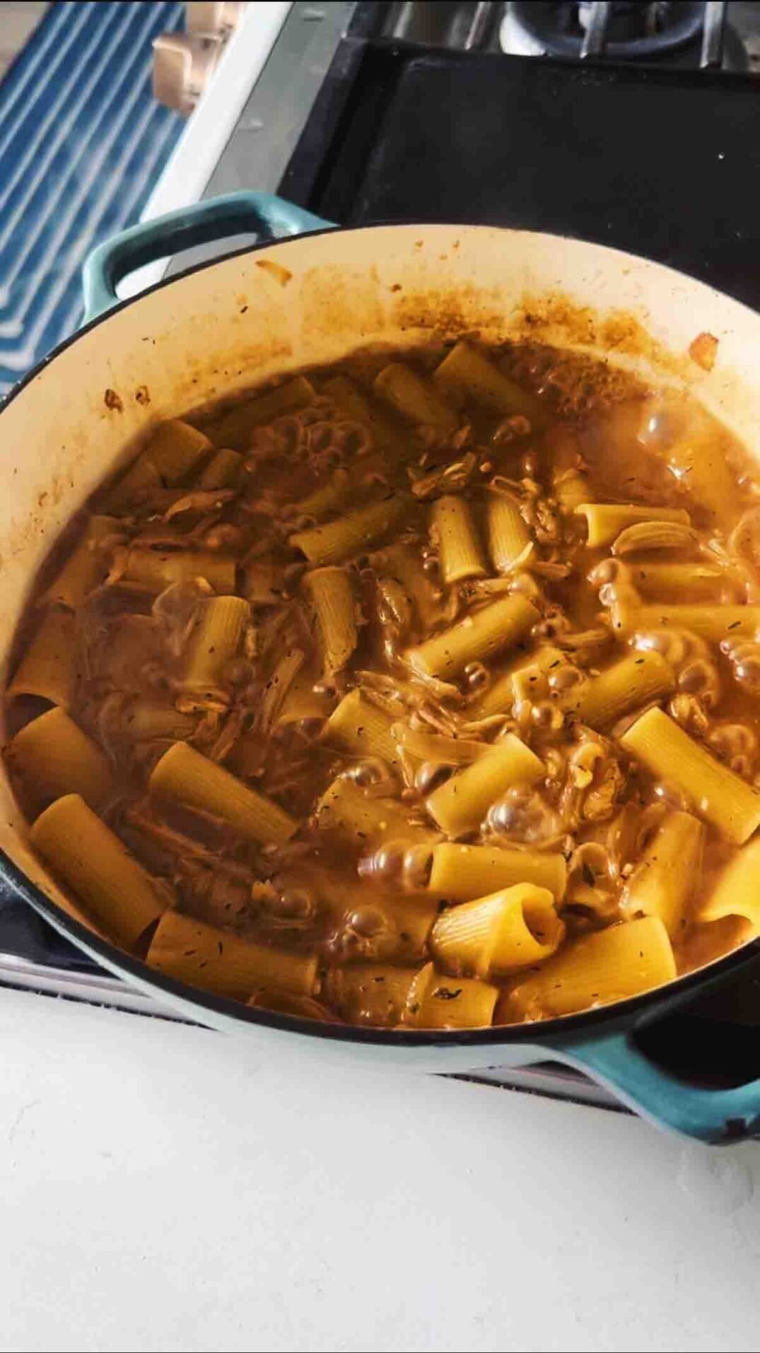 rigatoni boiling with caramelized onions on a stovetop.