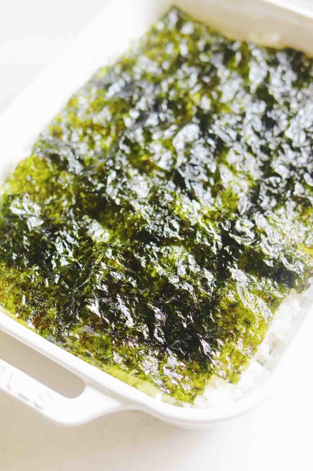 nori sheets on top of sticky sushi rice in a white staub baking dish.