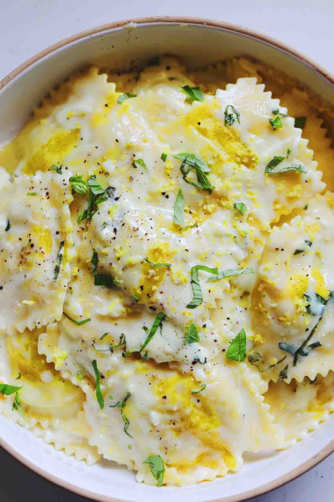 White and Yellow Corn Ravioli with basil in a creamy sauce in a white bowl.