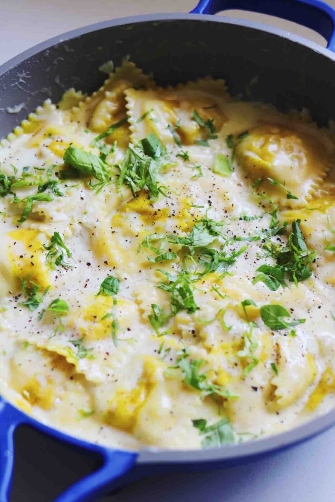 Trader Joe's Sweet Corn Ravioil in a blue our place pan with a creamy sauce with fresh basil on top.