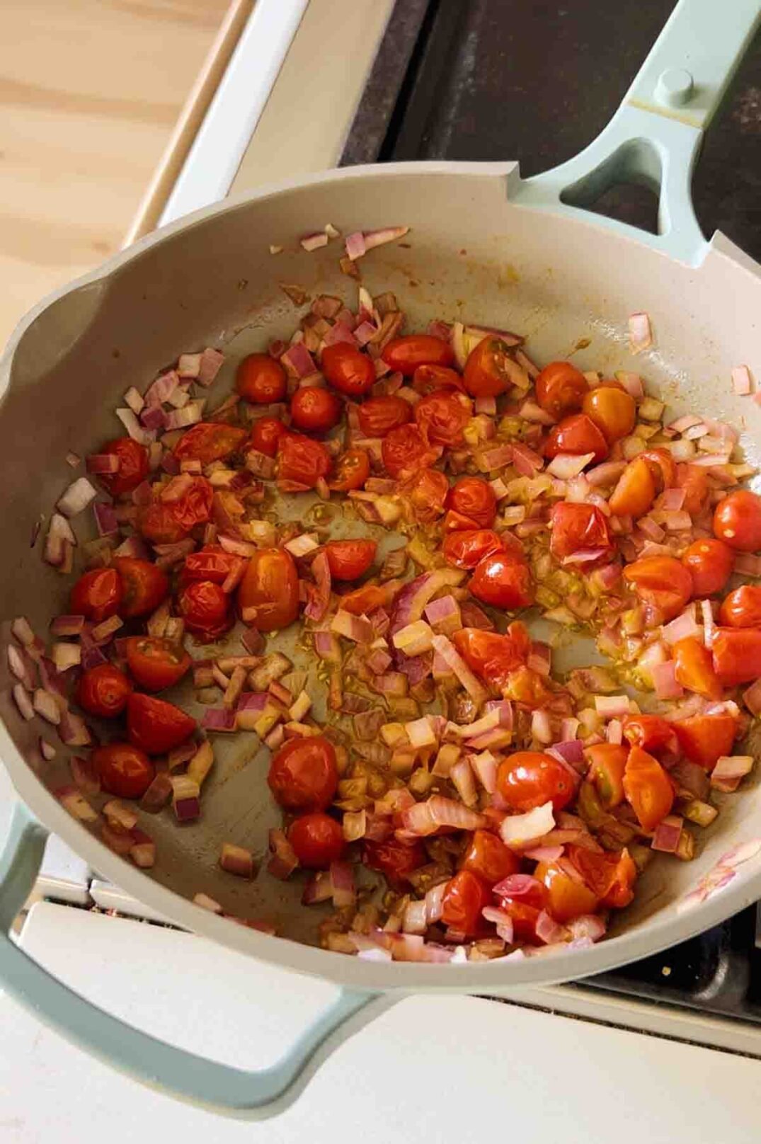 caramelized tomatoes and onions cooking in a blue pan.