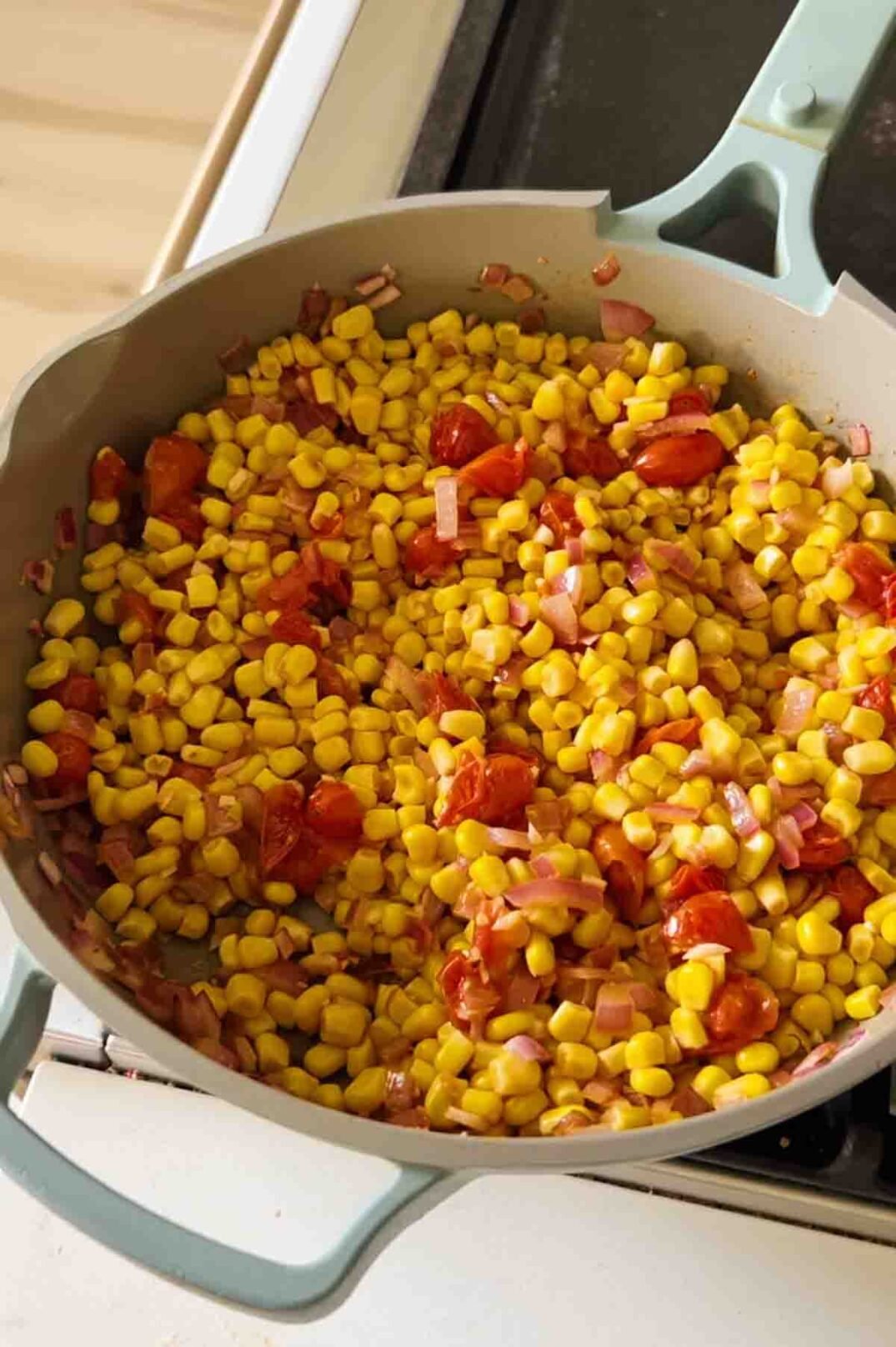 fresh corn, tomatoes, and onions cooking on the stovetop.