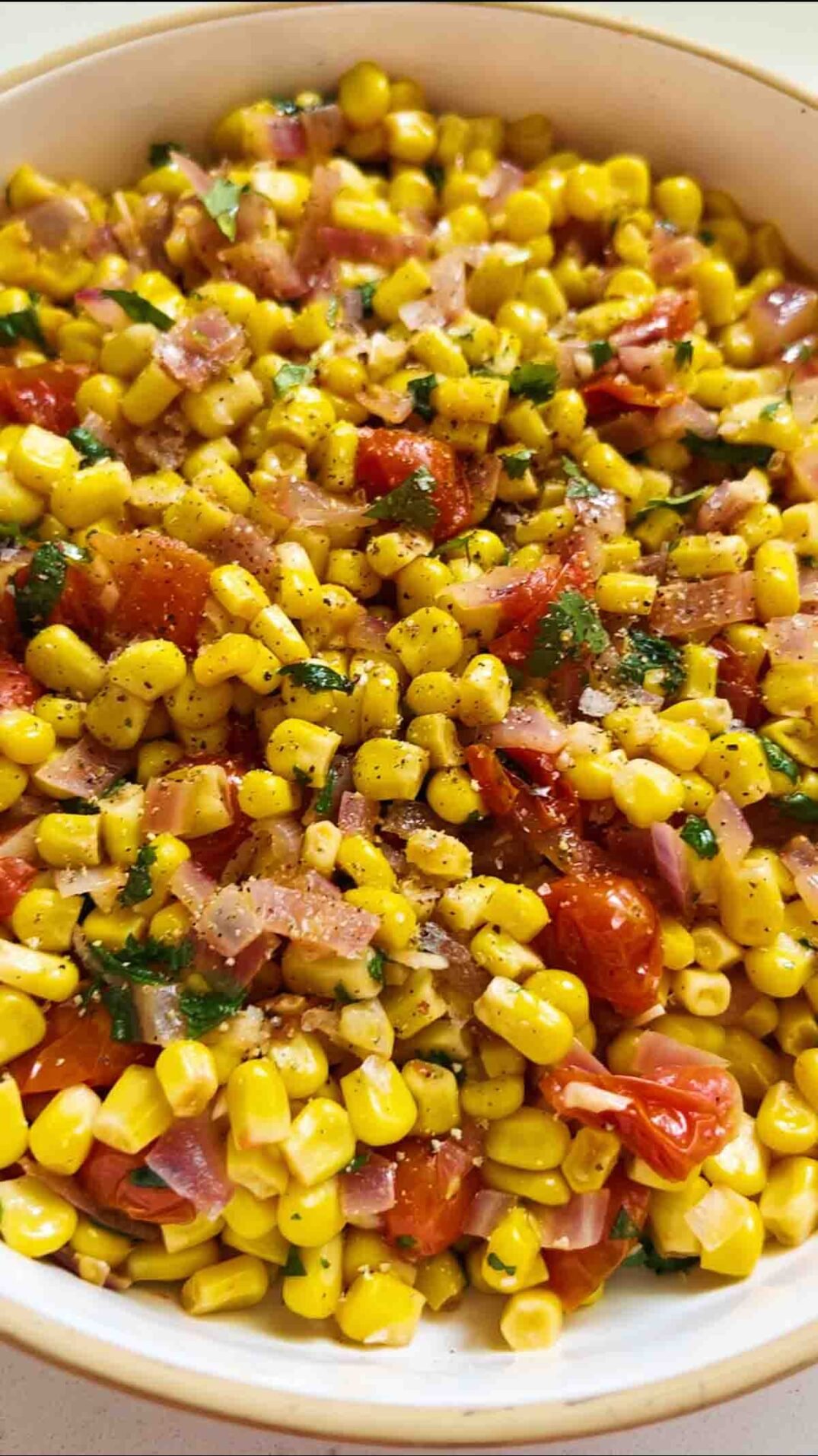 fresh corn, caramelized onions, tomatoes, cilantro and seasoning in a white bowl.