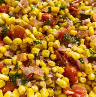 fresh corn, caramelized onions, tomatoes, cilantro and seasoning in a white bowl.