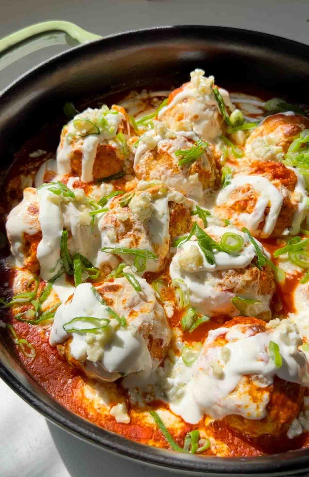 cheesy buffalo chicken meatball skillet with ranch dressing, scallions, and buffalo sauce.