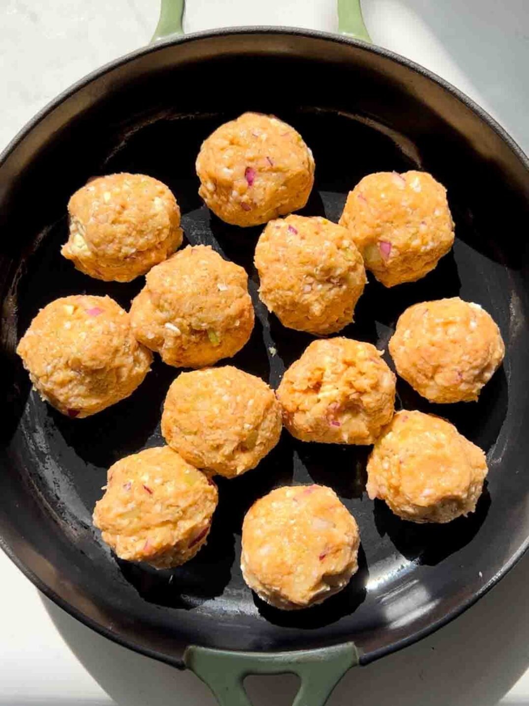 uncooked ground chicken meatballs in a green cast iron skillet.