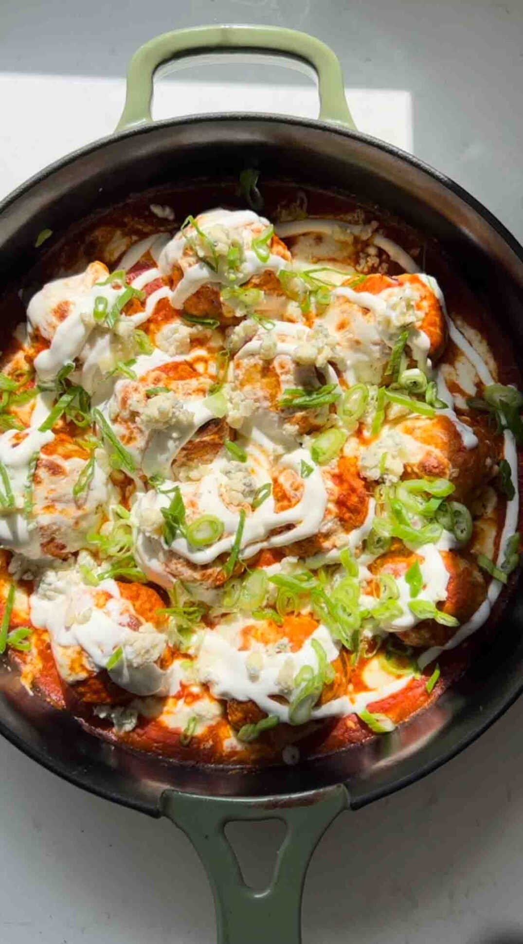 buffalo chicken meatballs covered with blue cheese, ranch dressing and scallions in a green cast iron skillet.