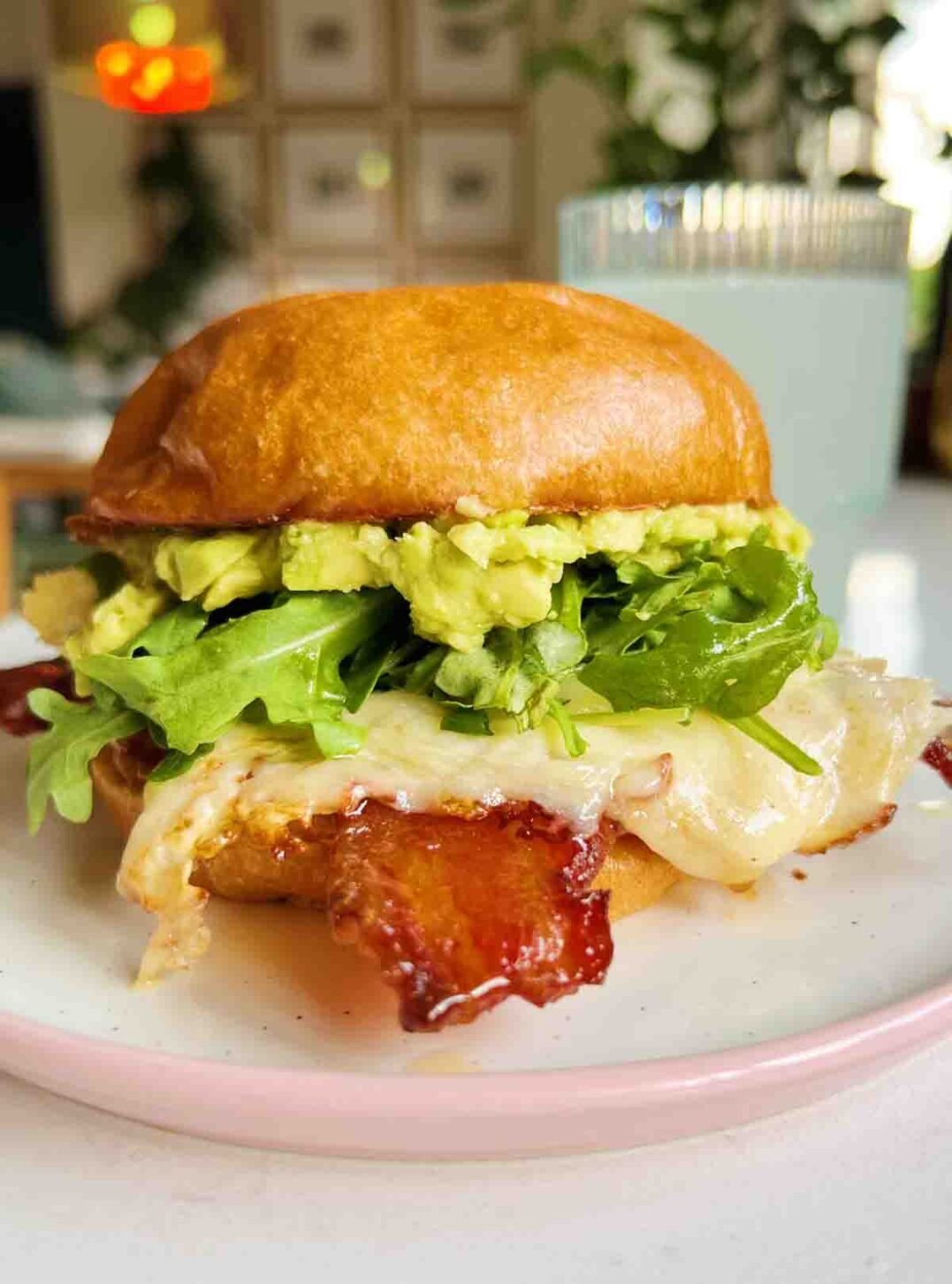 a colorful egg sandwich with arugula, bacon and avocado on a white plate.