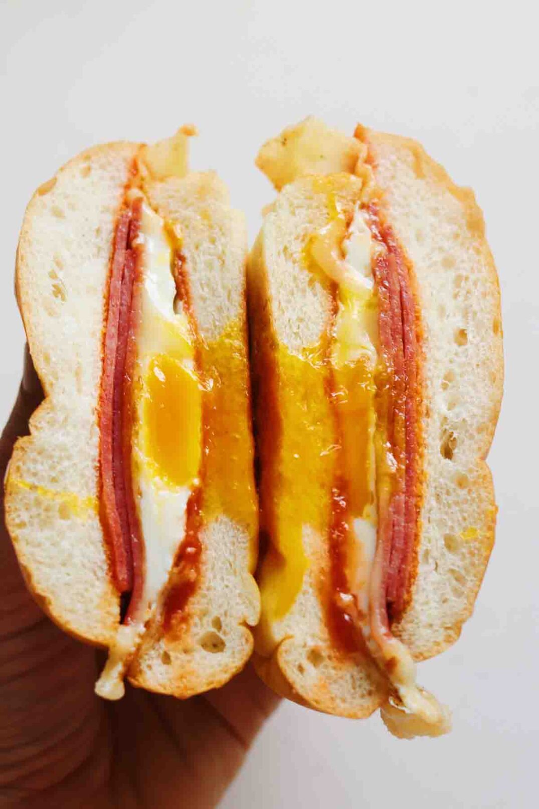 a hand holding a pork roll egg and cheese sandwich with egg yolk dripping out.
