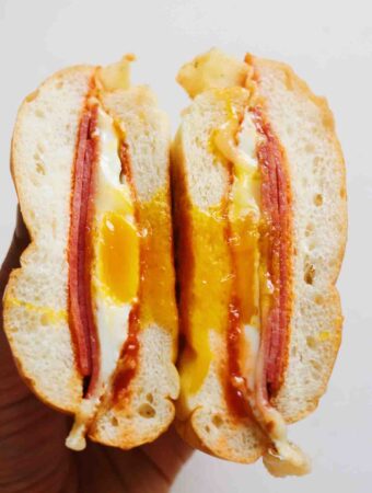 a hand holding a pork roll egg and cheese sandwich with egg yolk dripping out.