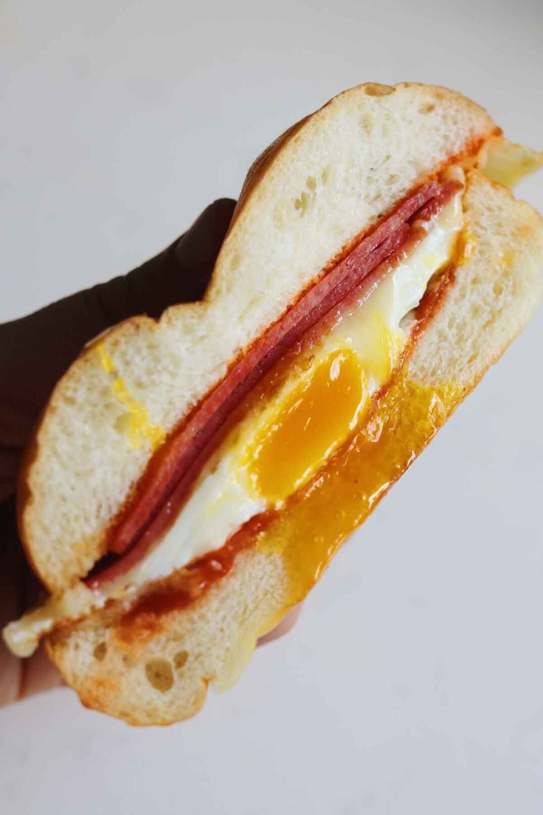 a half of a pork roll egg and cheese sandwich in someone's hand over a white background.