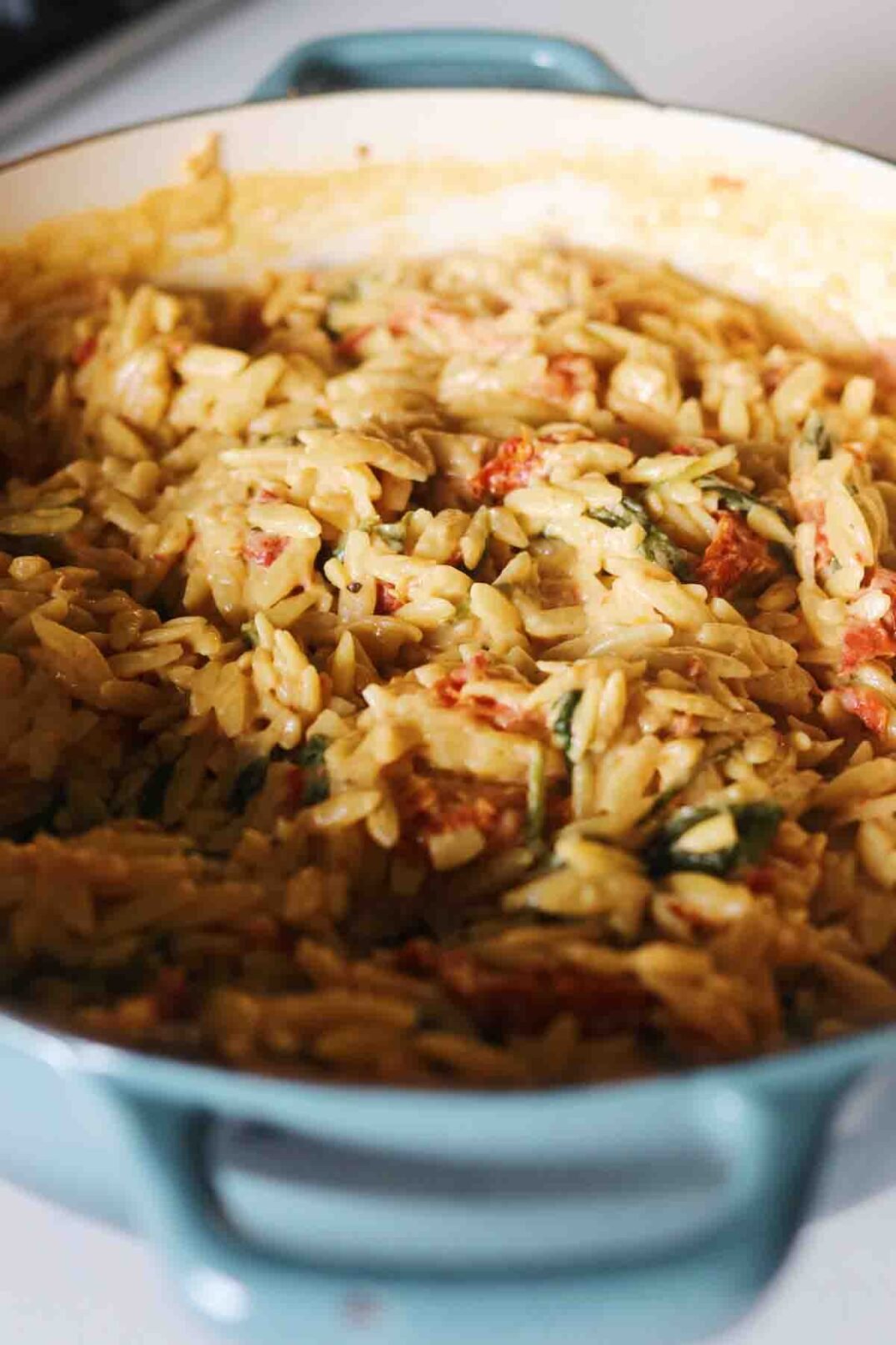 a ¾ view of a big pot of golden sun dried tomato orzo.
