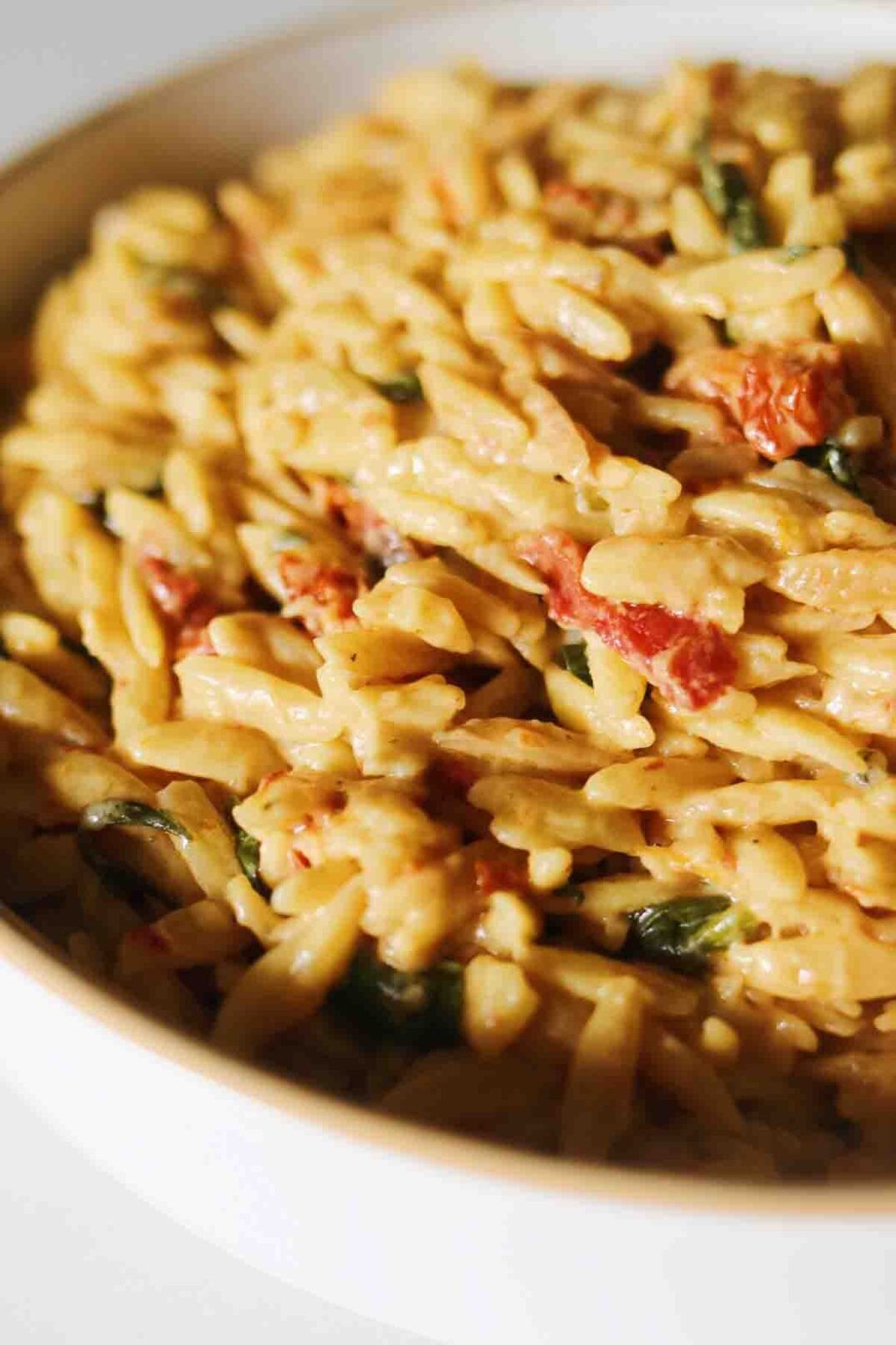 an up close view of a white bowl filled with spinach and sun dried tomato orzo.