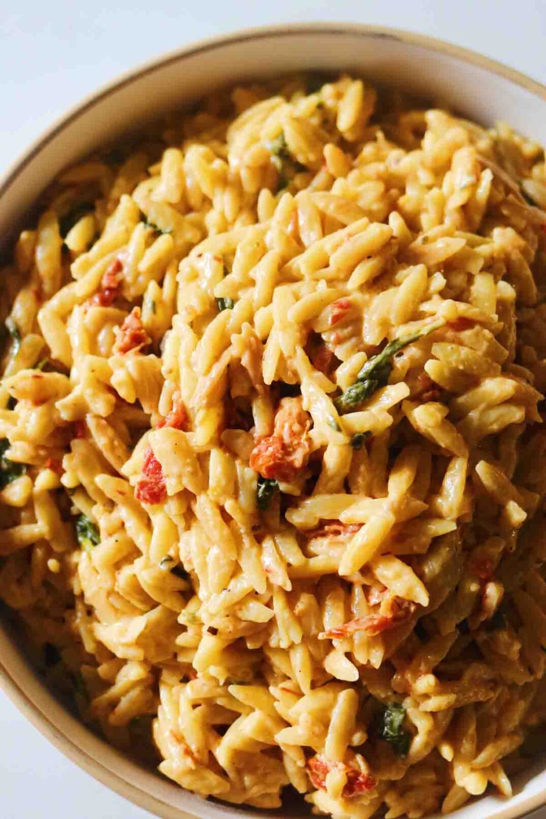 creamy orzo with specks of spinach and sun dried tomatoes in a white bowl.