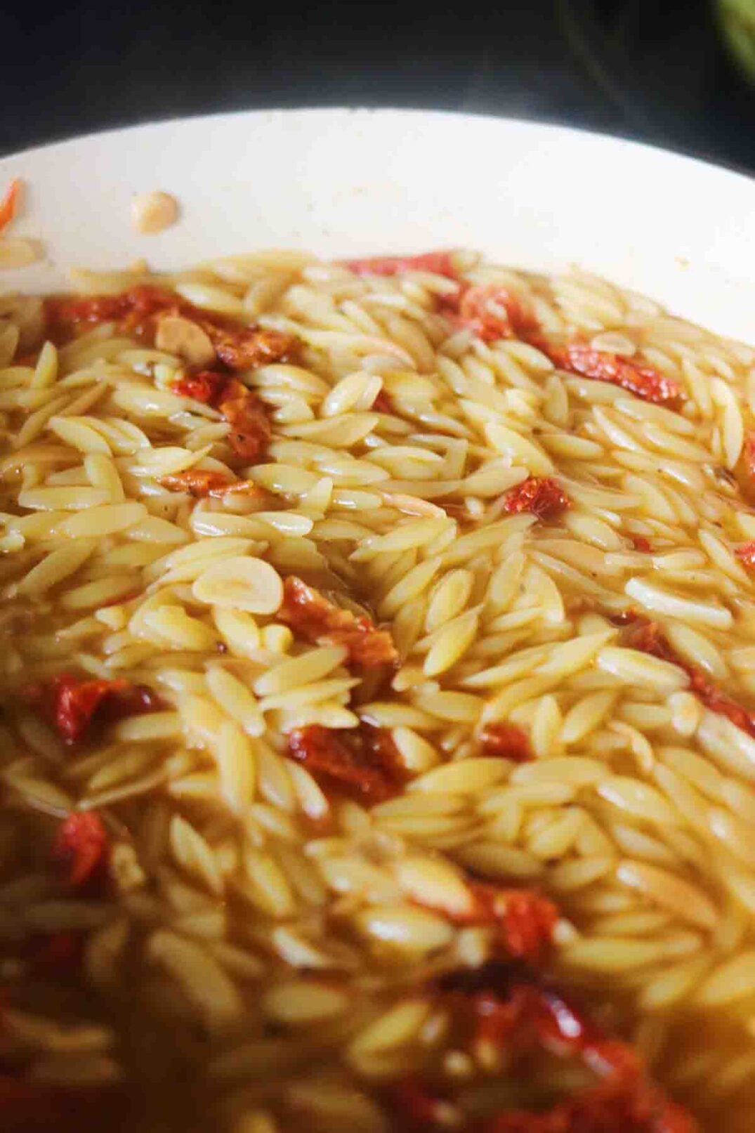 orzo and sun dried tomatoes cooking in a soupy broth.