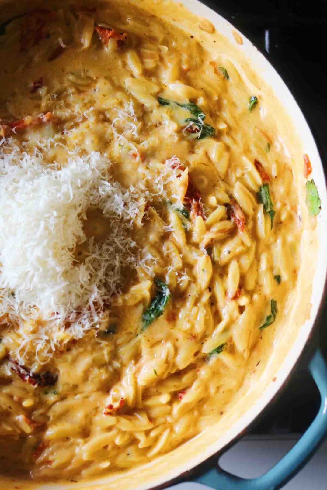 an overhead view of creamy sun dried tomato orzo with grated parmigiano on top.