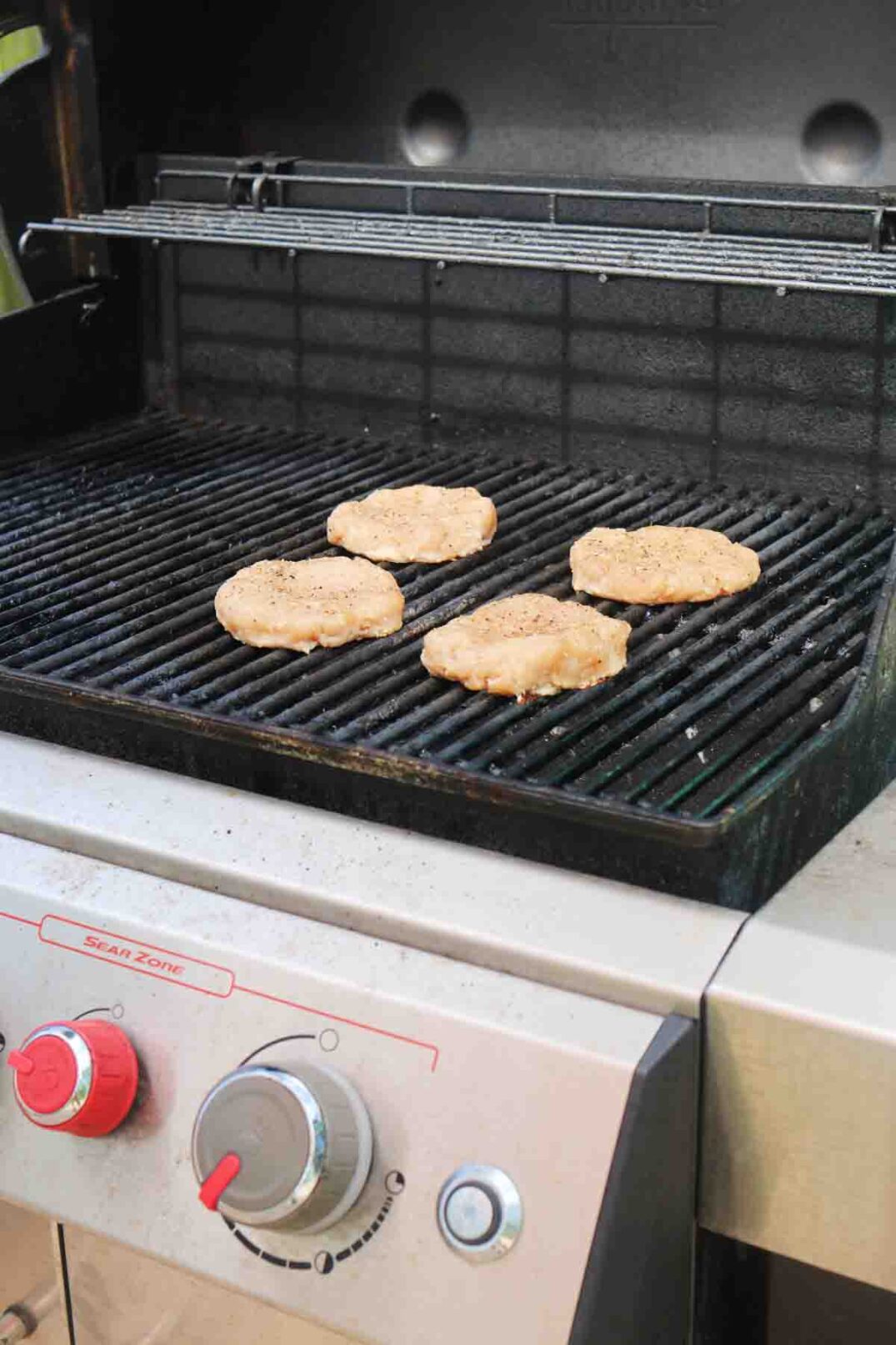four uncooked turkey burger patties sitting on a silver grill.