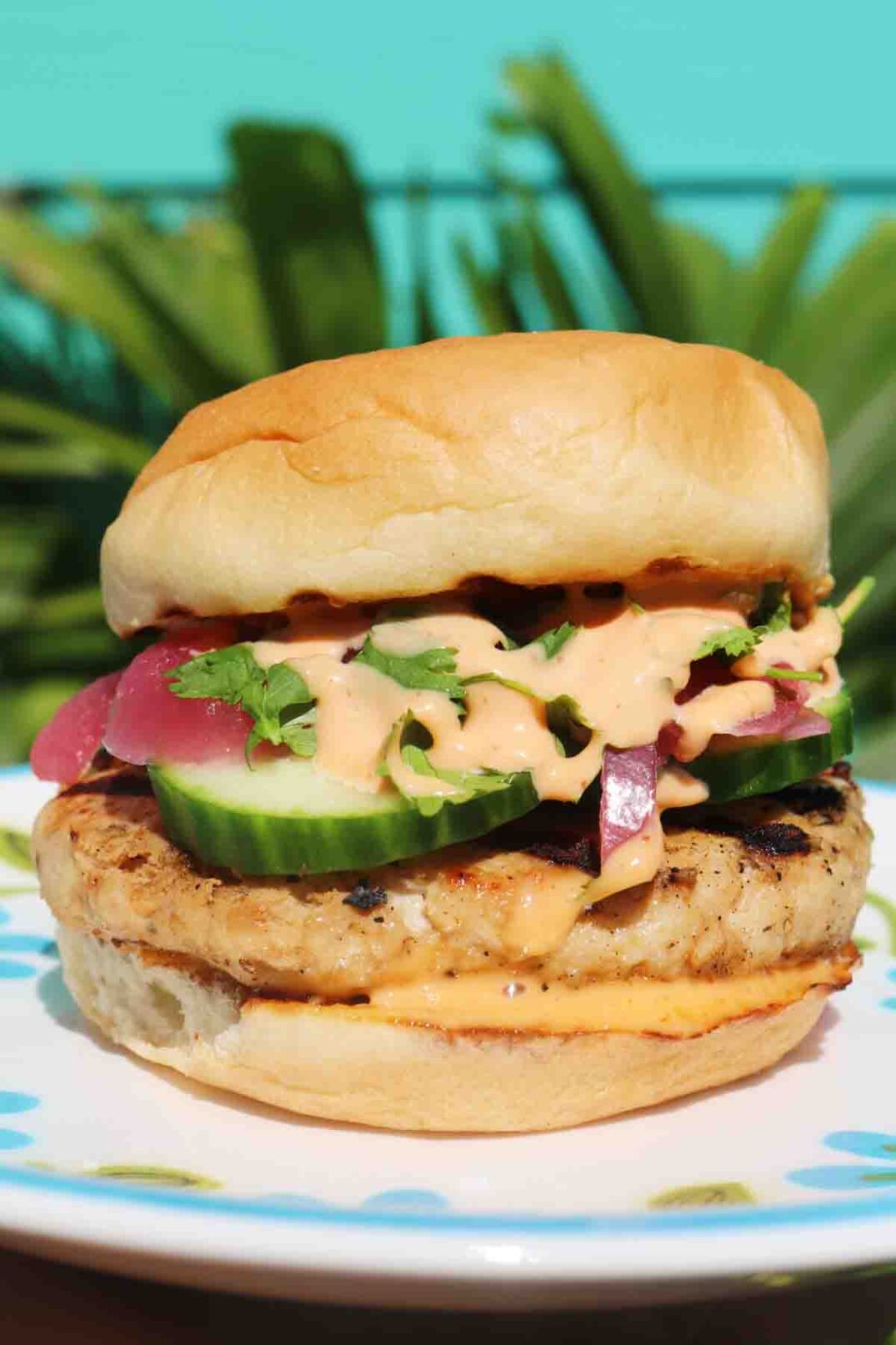 an up close view of a tropical teriyaki turkey burger with a palm tree in the background.