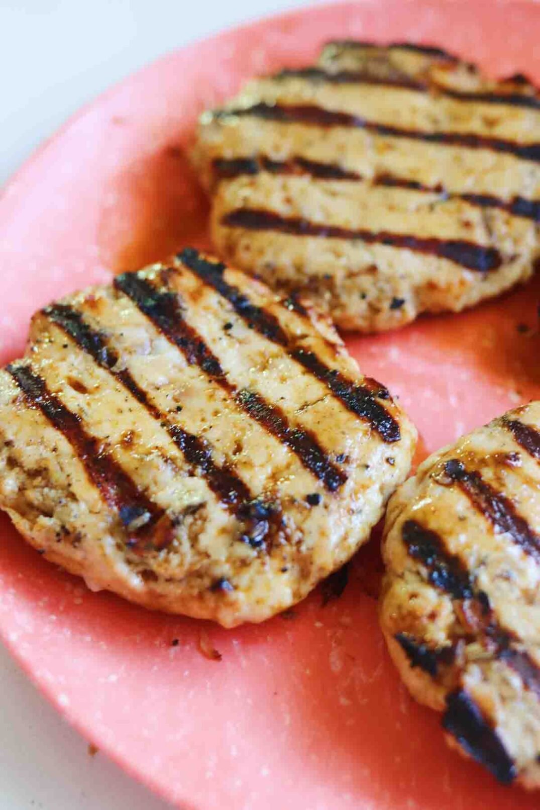 cooked turkey burgers with grill marks on a pink plate.