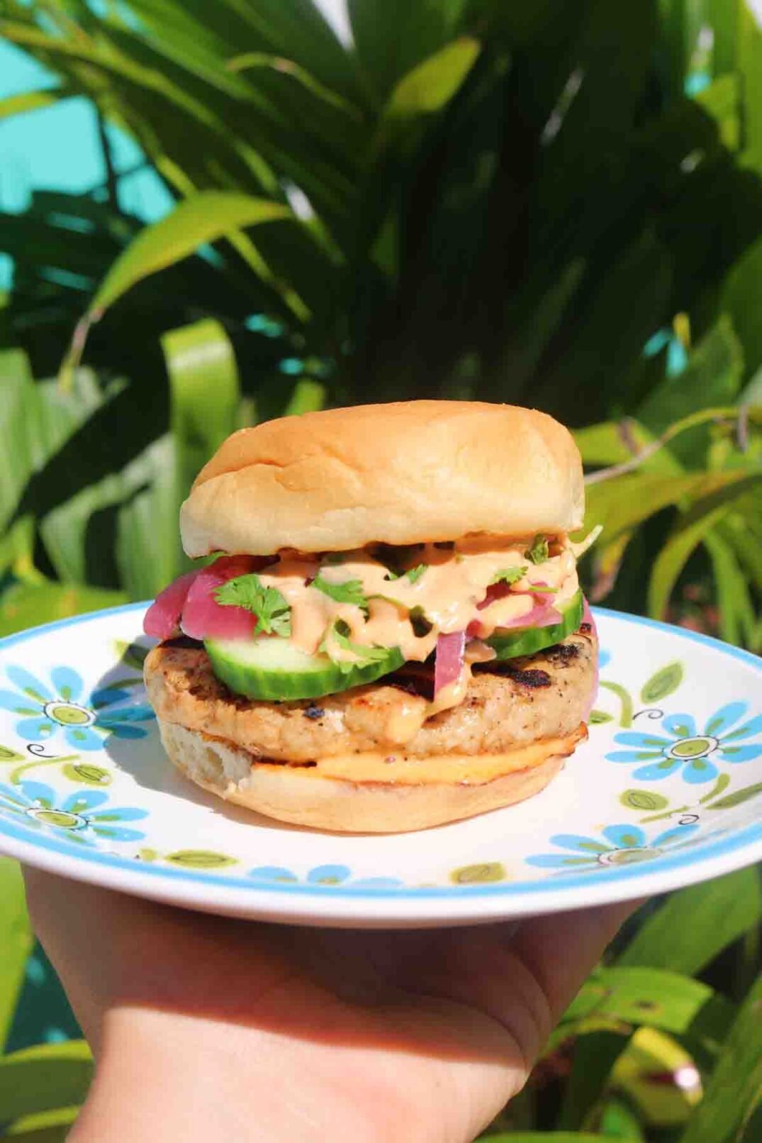 a teriyaki turkey burger in front of a bright green palm tree.