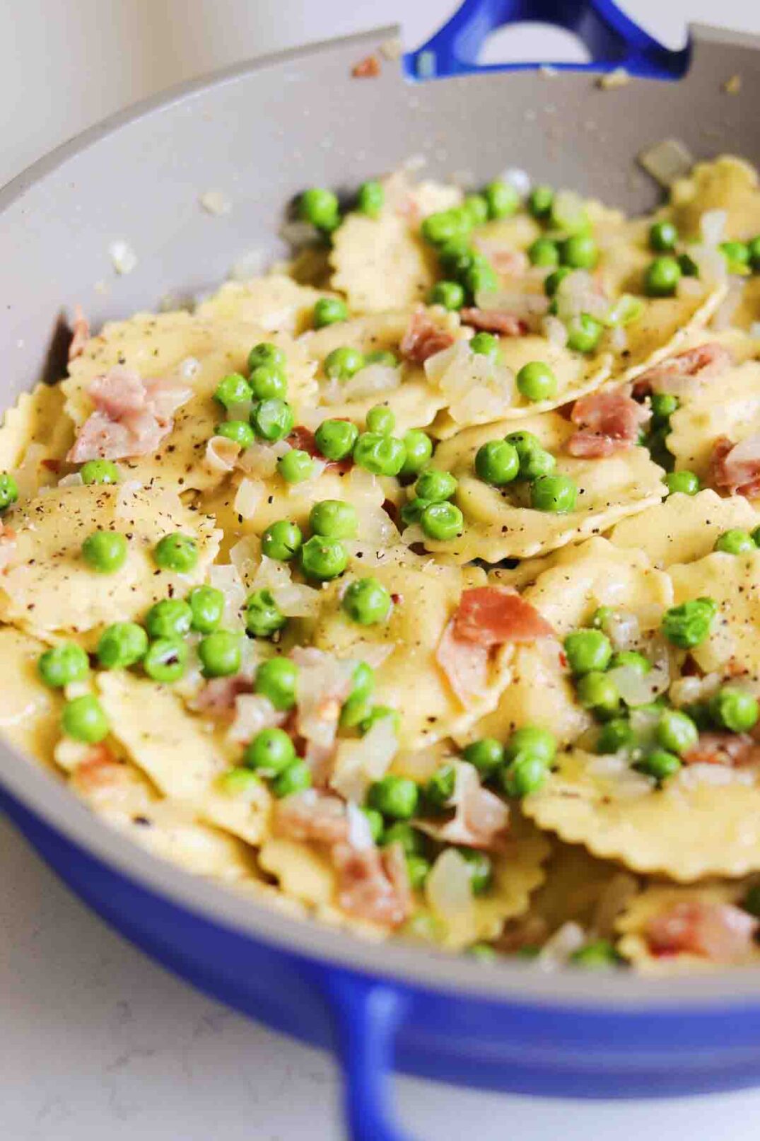 a blue our place always pan filled with Trader Joe's Cacio e Pepe Ravioli, peas, and crispy prosciutto.