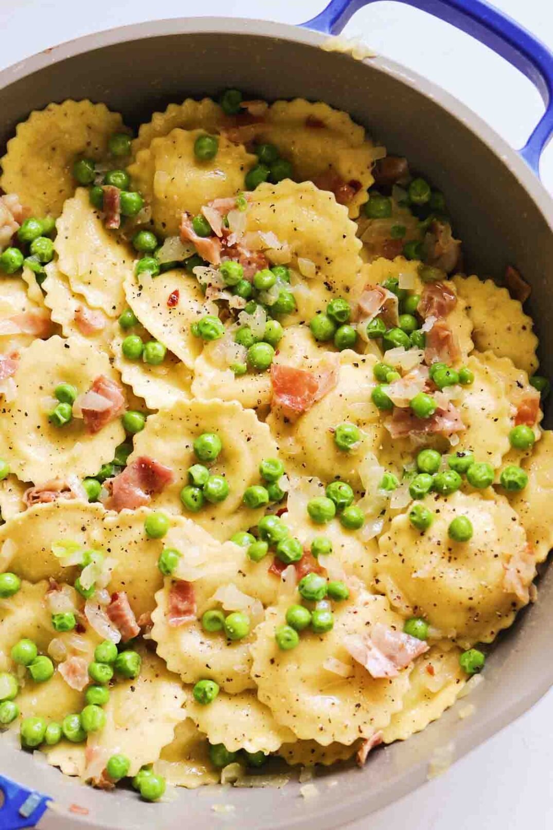 a nonstic pan filled with savory italian ravioli, green peas, crispy pink prosciutto.