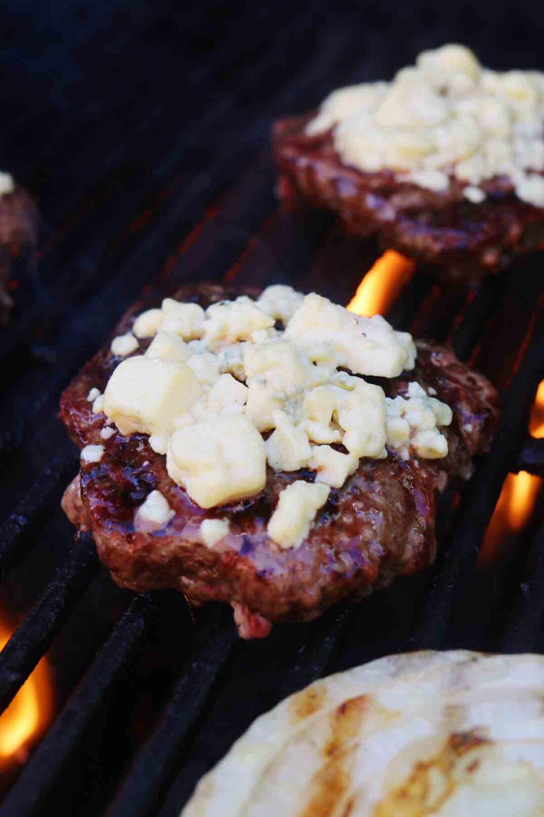 blue cheese crumbles melted onto a beef patty on a grill top.