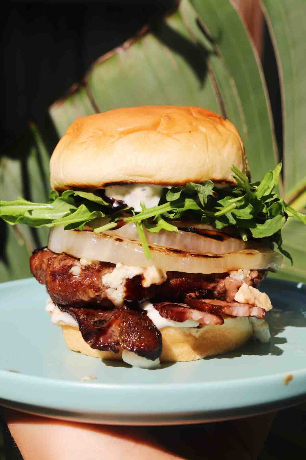 a beatufiul burger on a blue plate in front of a palm tree.