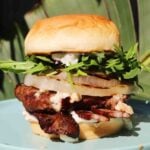 a beatufiul burger on a blue plate in front of a palm tree.