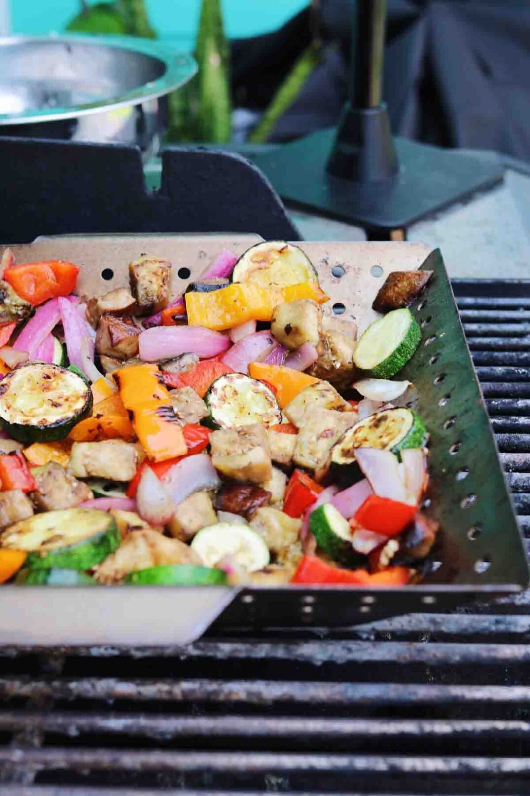 a metal grill basket full of colorful veggies on a hot grill.