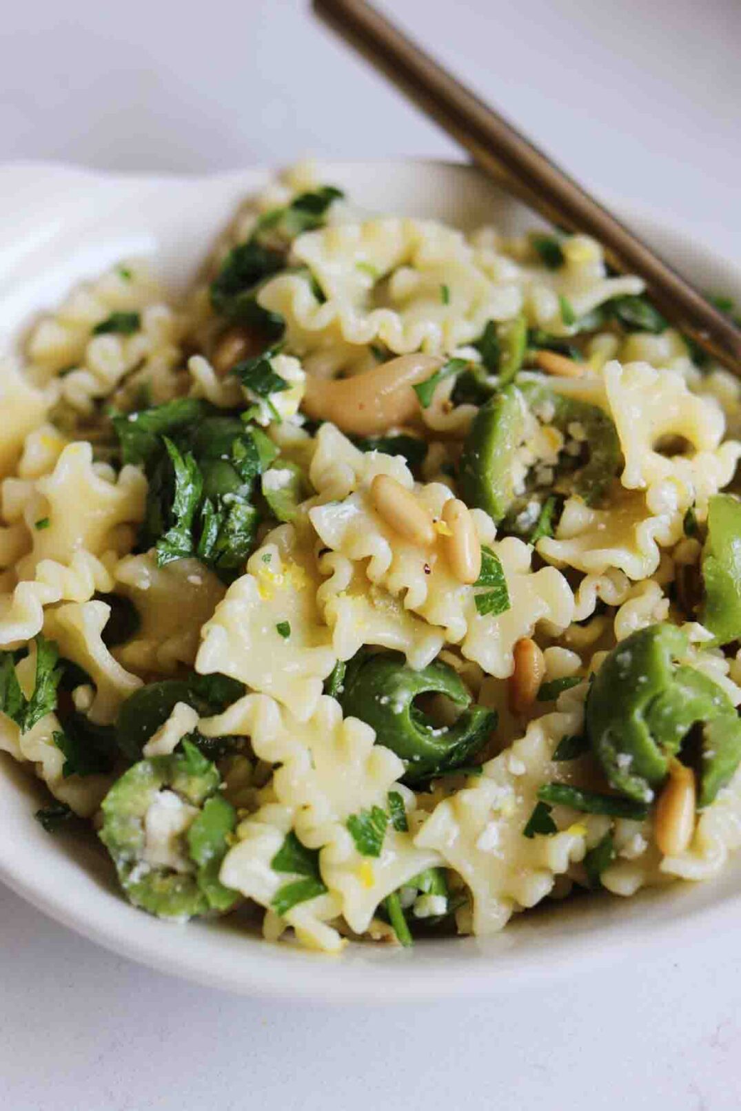 pasta, olives, parsley, pine nuts and blue cheese tossed together and scooped into a bowl.
