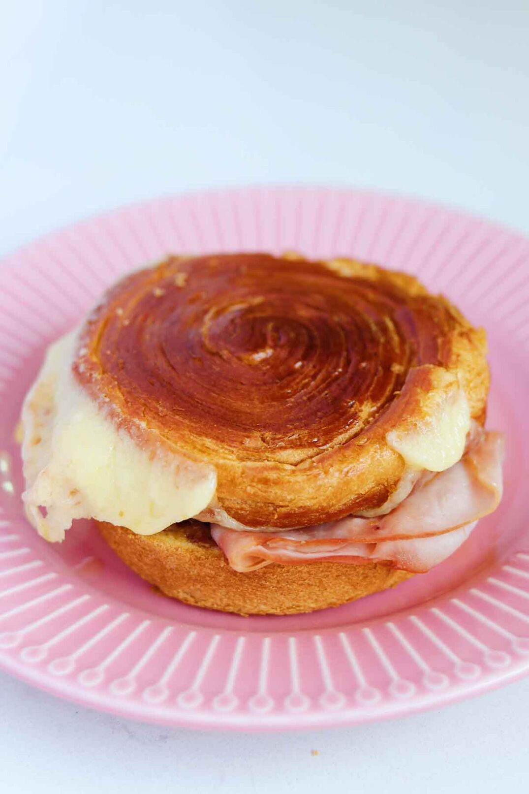 a ham and cheese croissant bun sitting on  pink plate on a white countertop