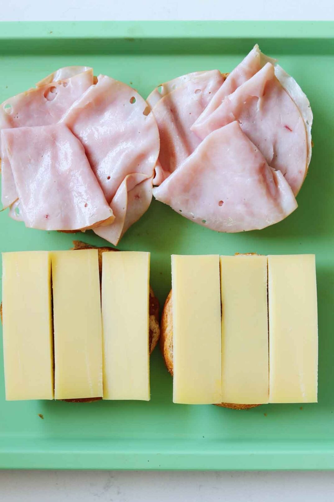 slices of comte and ham on top of a croissant bun on a green baking sheet.