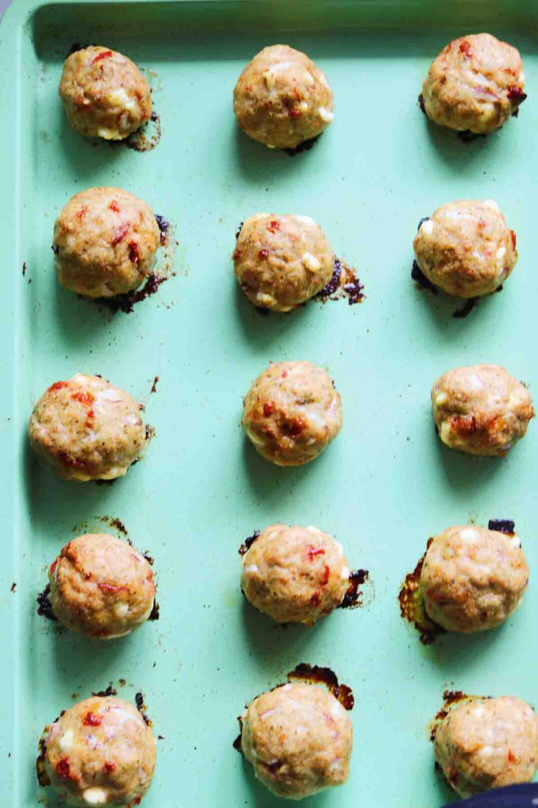 cooked chicken meatballs on a green baking sheet.
