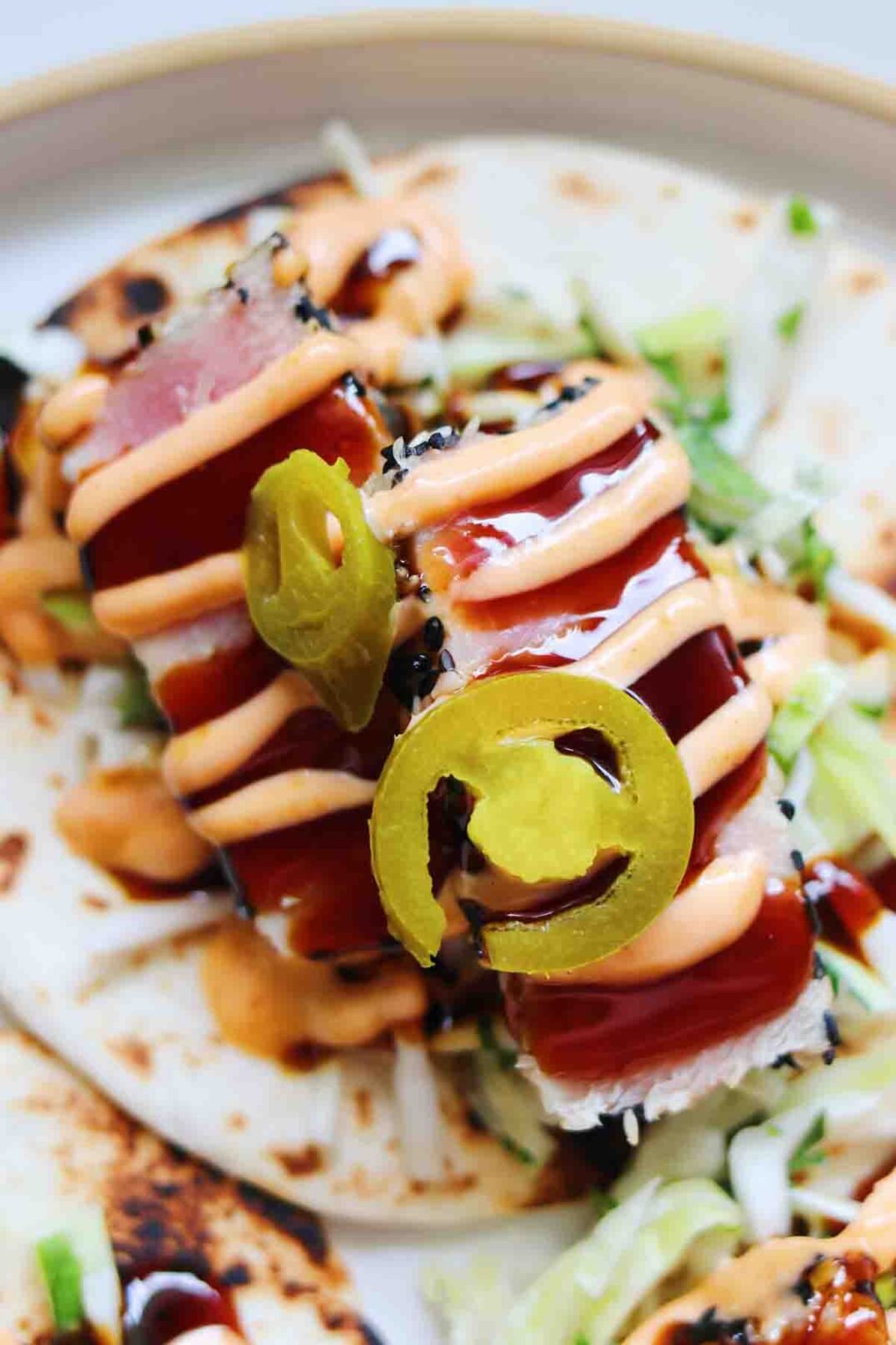 a single ahi tuna taco on a white plate drizzled with eel sauce and spicy mayo.