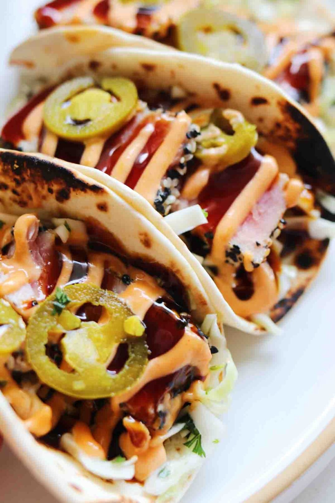 3 folded tuna tacos drizzled with sauce and green pickled jalapenos.